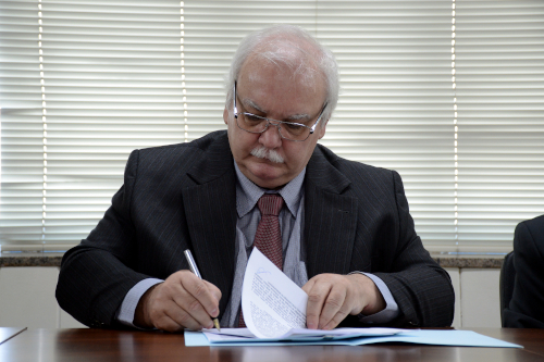 Presidente, de terno preto , sentado assinando termo.