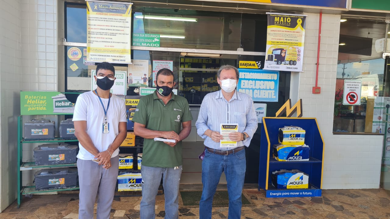 servidor Ariel, motorista Wilson e o desembargador exibem panfletos, todos com máscara, ao fundo cartazes no posto de combustíveis