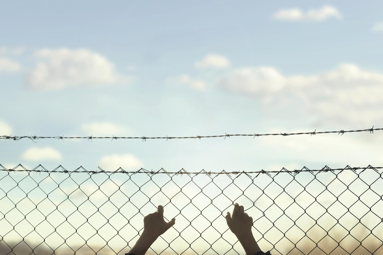 Mãos segurando alambrado com céu ao fundo.
