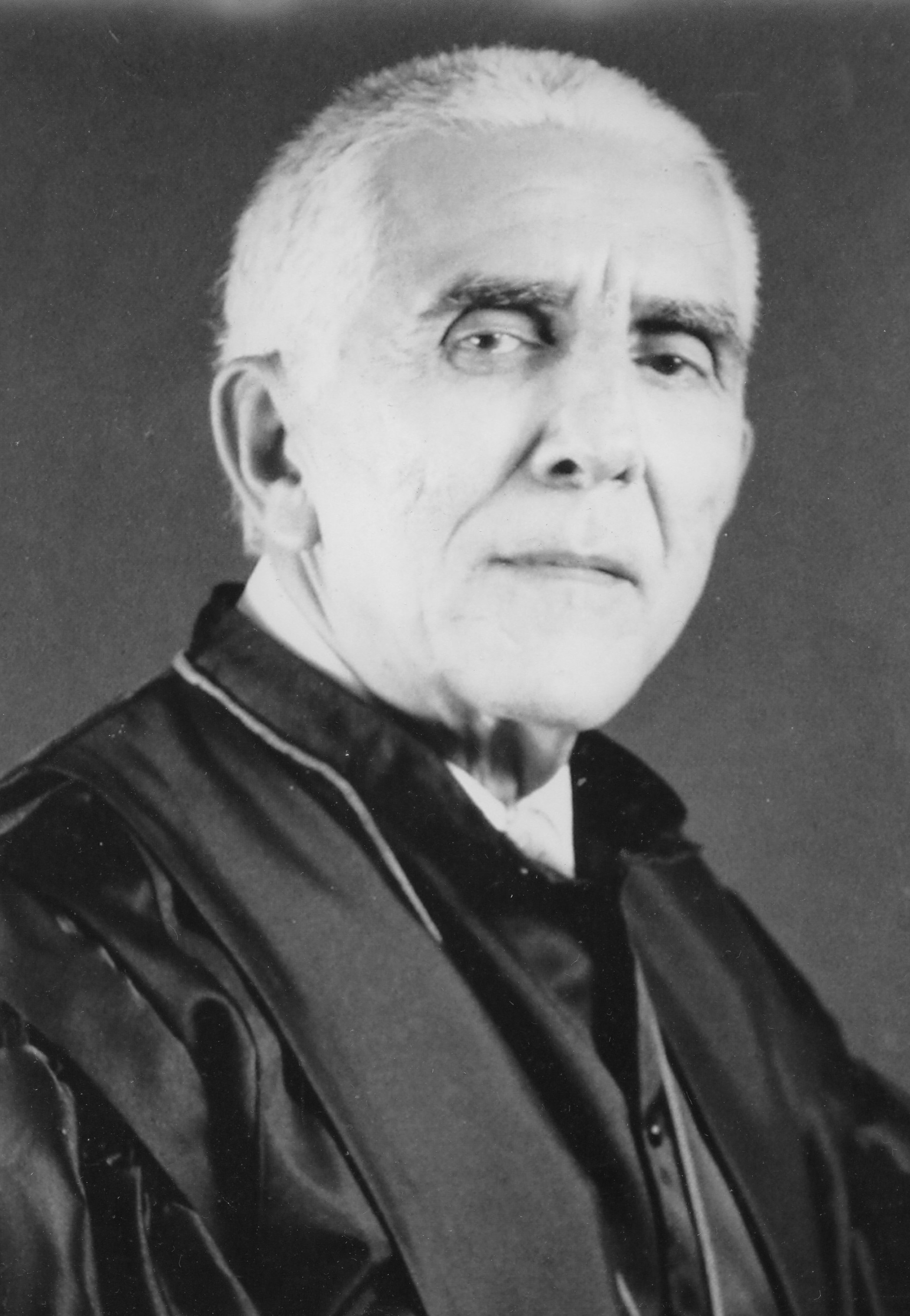 Fotografia em preto e branco, homem branco, cabelo branco, usando toga.