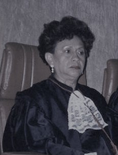 Fotografia em preto e branco, mulher branca, cabelo preto, usando toga.